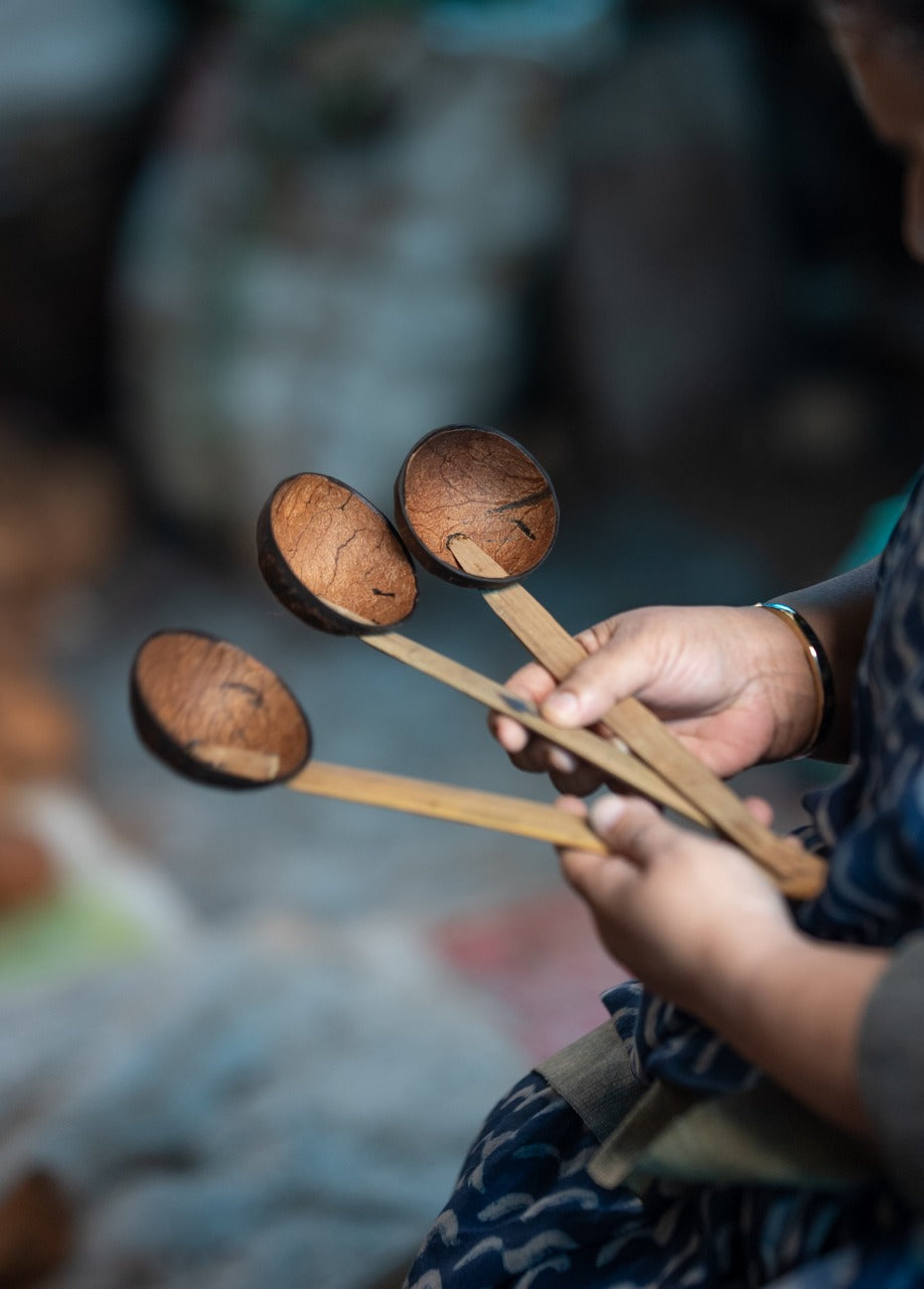 A person holding three coconut shell spoons with long bamboo handles.