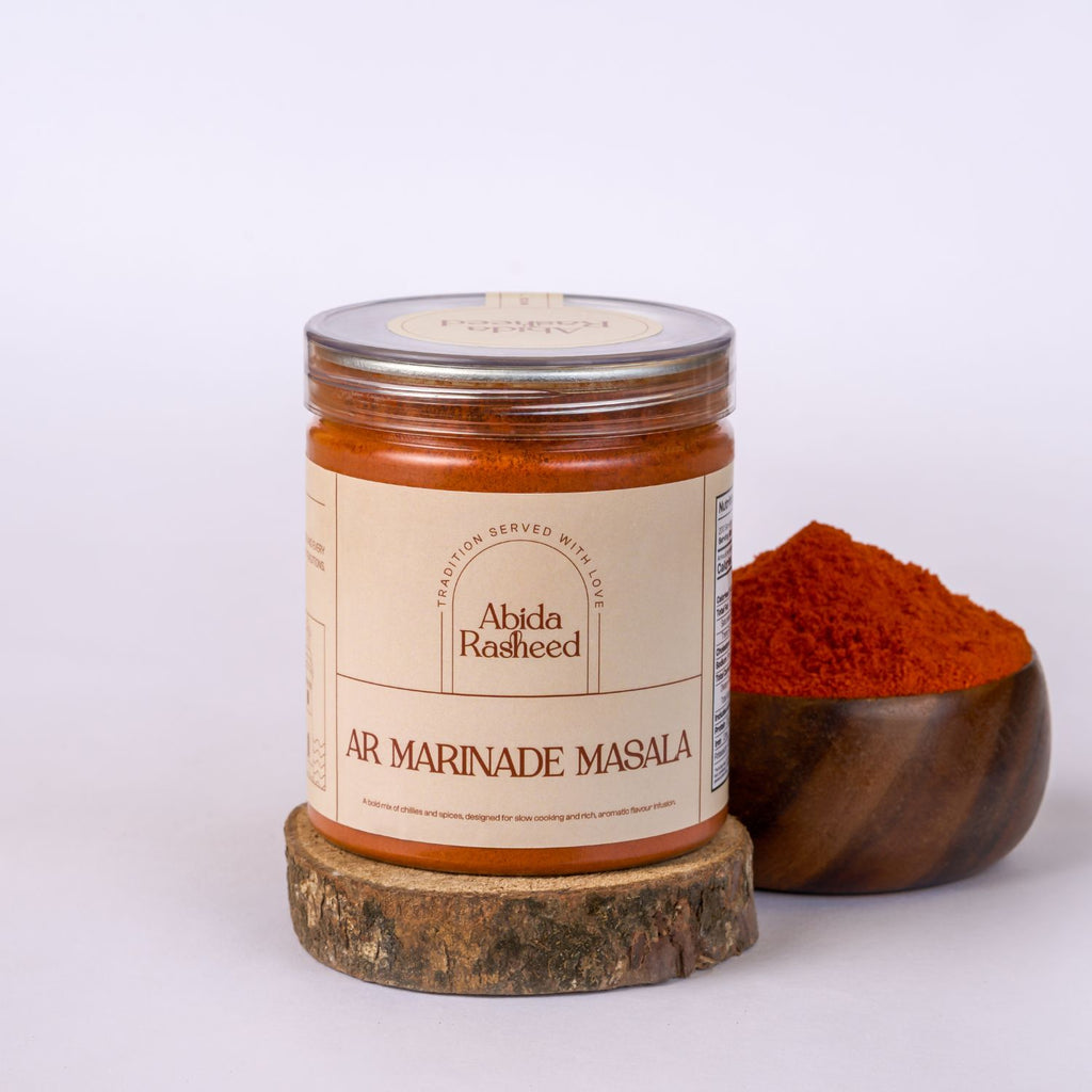 Jar of Abida Rasheed AR Marinade Masala with a wooden bowl of spices on a white background